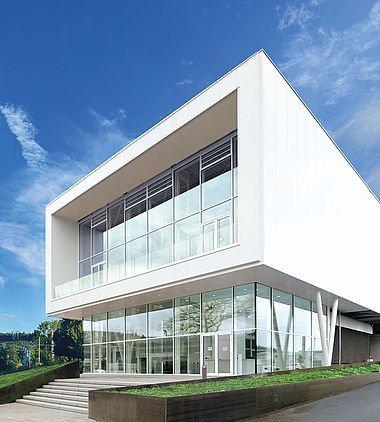 Modernes weißes Bürogebäude mit Glasfassade unter klarem blauen Himmel