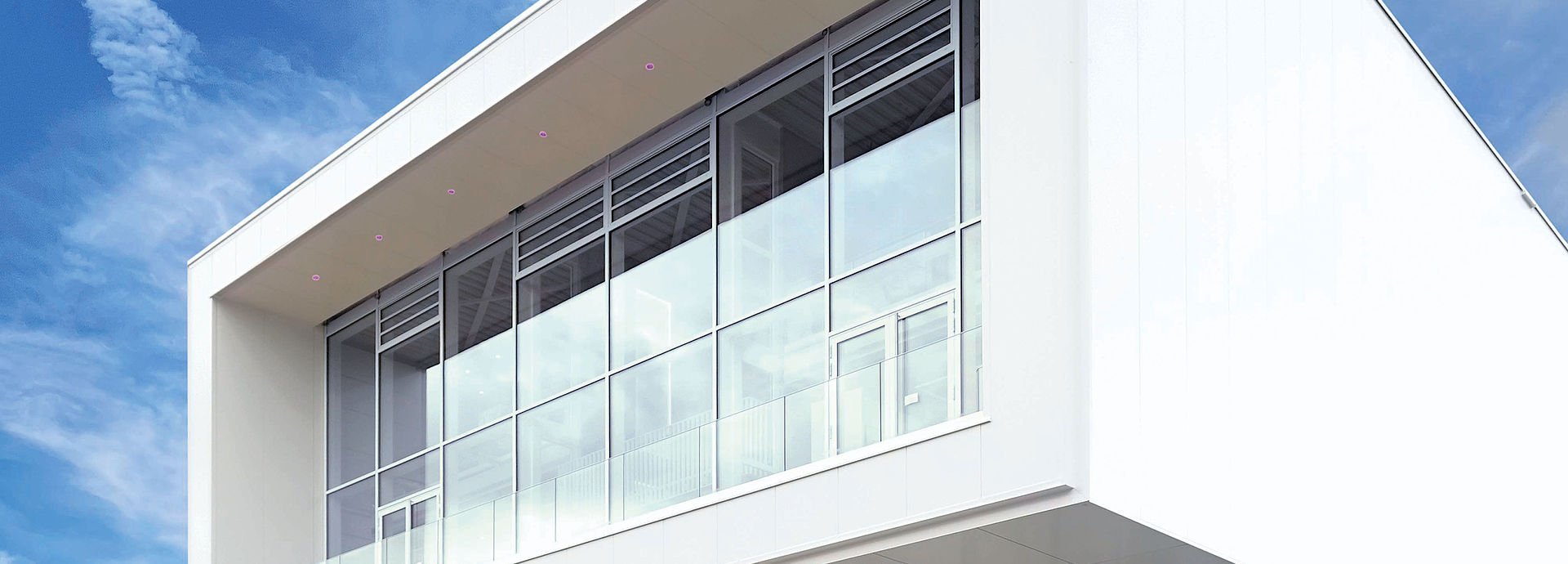 Modernes weißes Bürogebäude mit Glasfassade unter klarem blauen Himmel